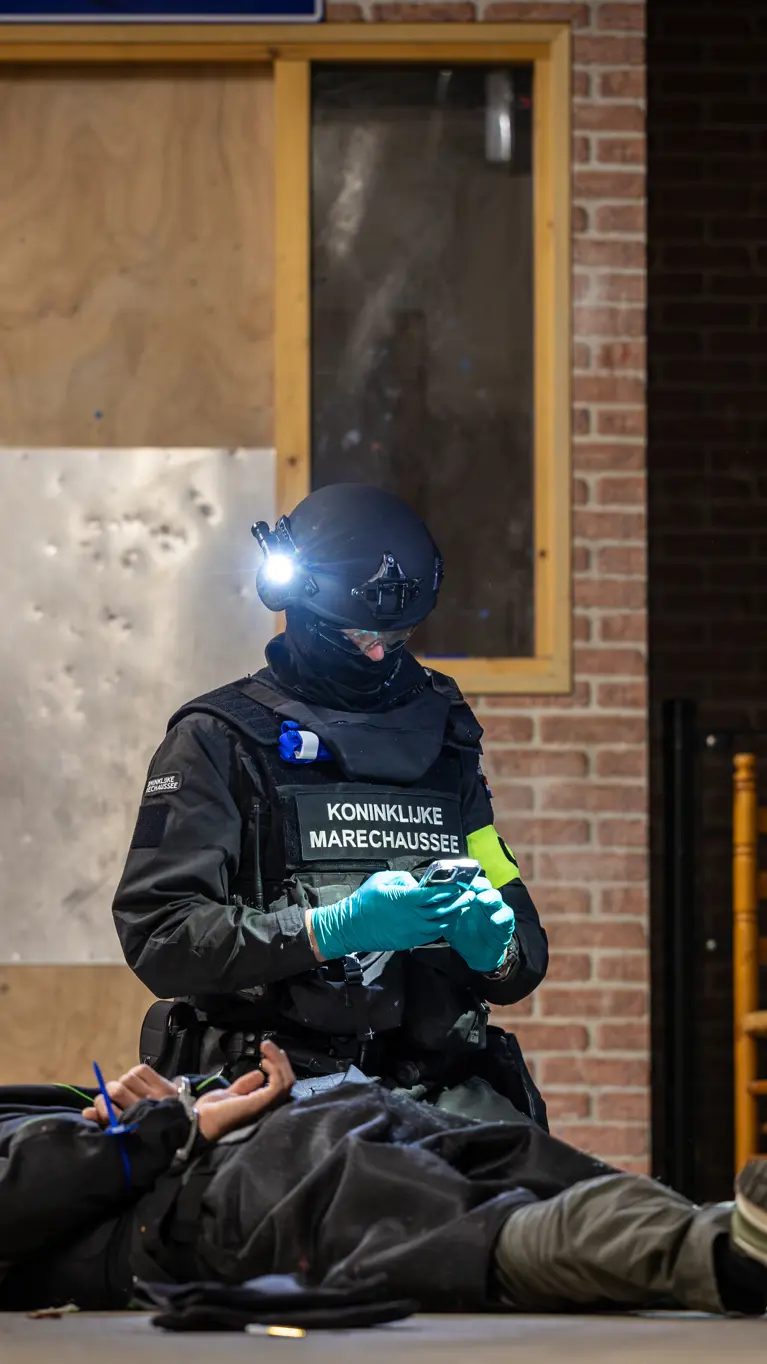 Een verdachte ligt geboeid op de grond met twee marechaussees om hem heen.