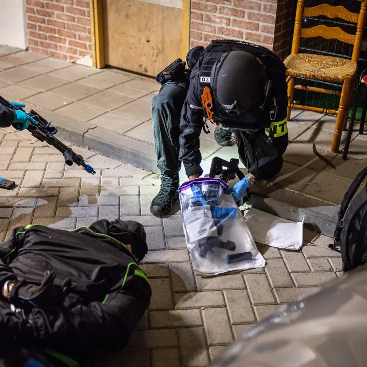 Terwijl de verachte op de grond ligt, stelt een marechaussee het wapen veilig.
