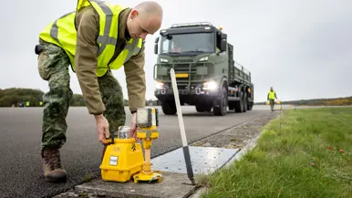 Iemand in een geel hesje plaatst een lamp op het asfalt. Op de achtergrond is een Scania vrachtwagen te zien.&nbsp;