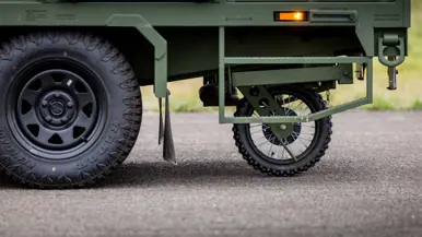 Een wieltje onder een groene aanhangwagen, van dicht bij de grond bezien.&nbsp;