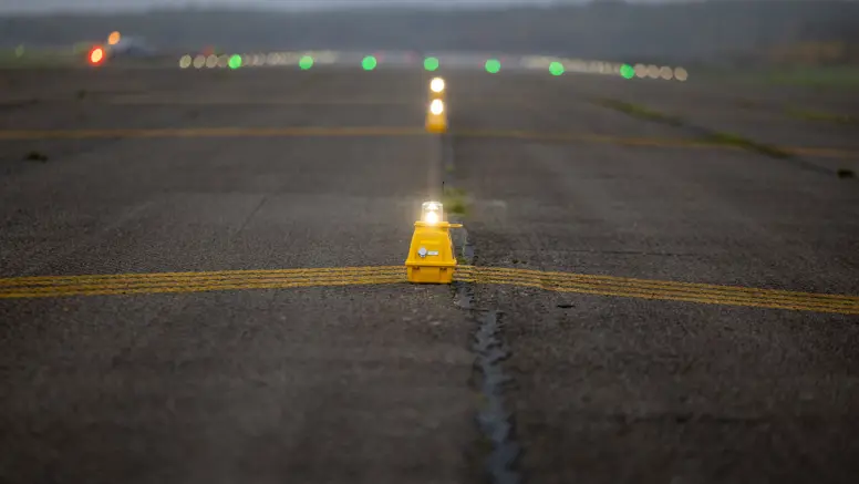 Een lamp met een gele onderkant op een landingsbaan. Erachter staan op het asfalt nog meerdere grote lampen opgesteld.&nbsp;
