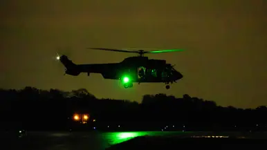  Een landende Cougar in de duisternis. In de verte zijn de landingsbaanlichten te zien.  