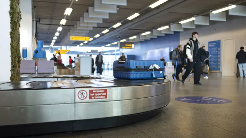 Blauwe koffer op een kofferband op Eindhoven Airport.