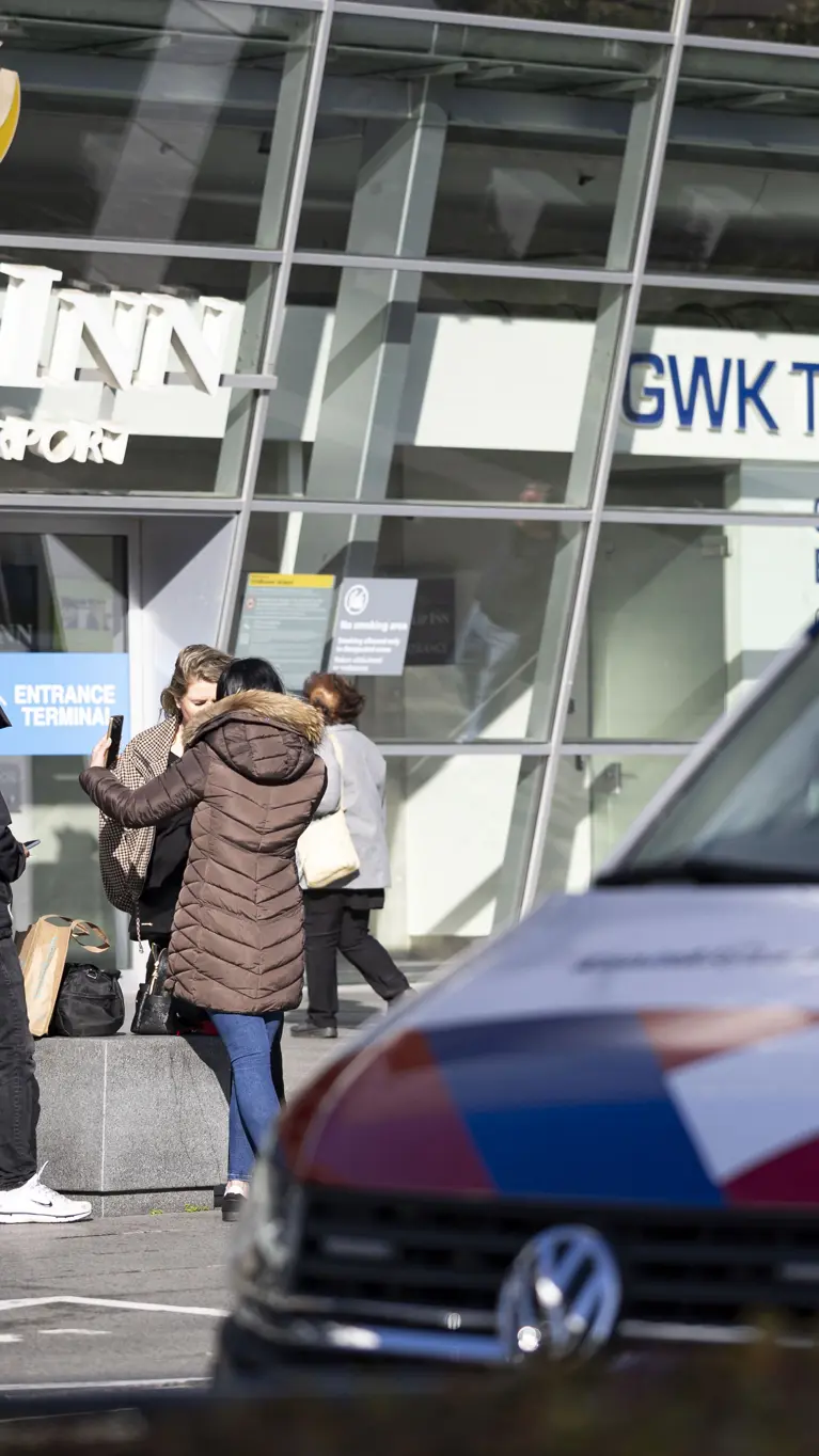 Voertuig van de KMar op Eindhoven Airport, op de achtergrond agenten in burger die met een vrouw praten.