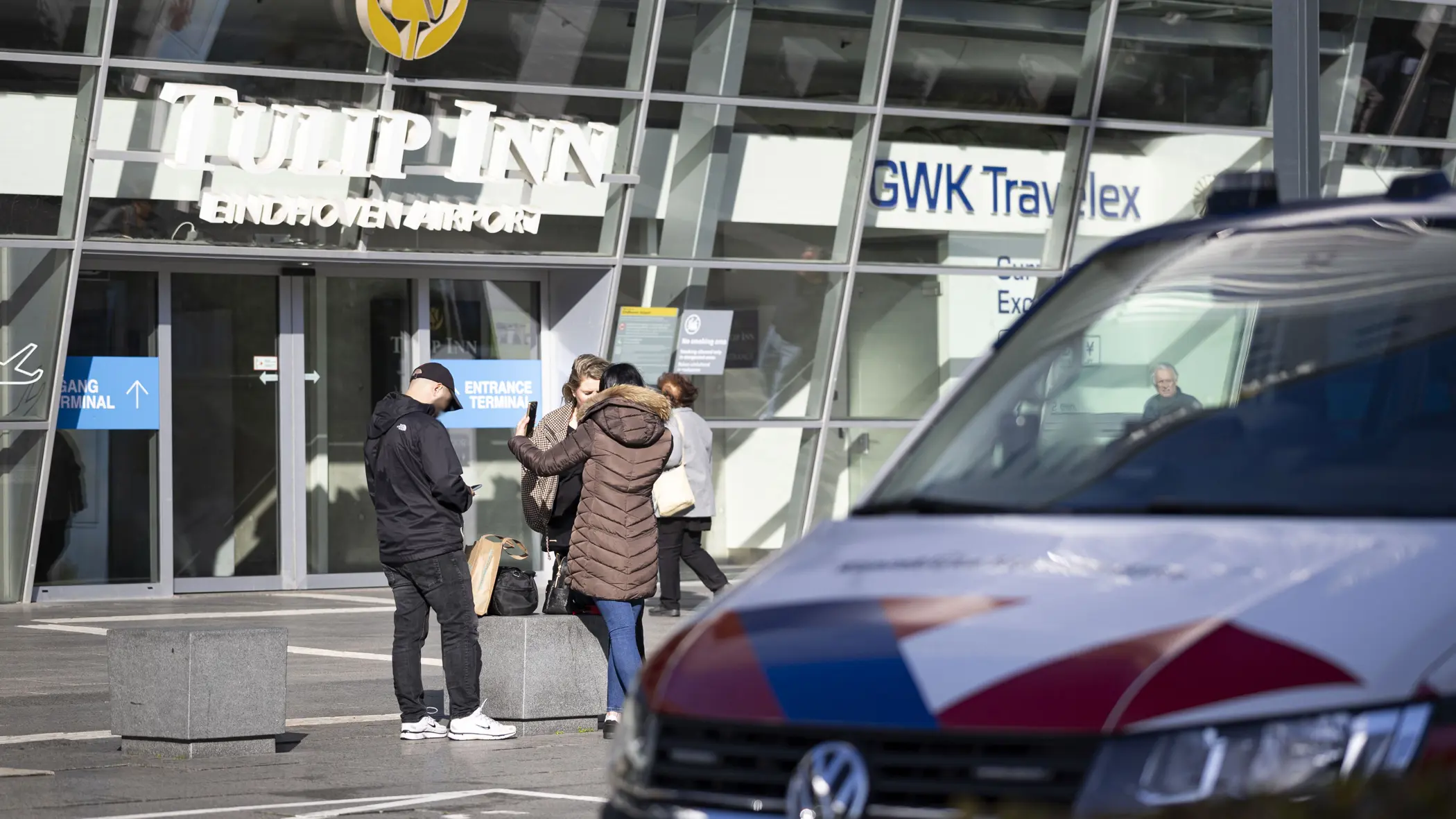 Voertuig van de KMar op Eindhoven Airport, op de achtergrond agenten in burger die met een vrouw praten.