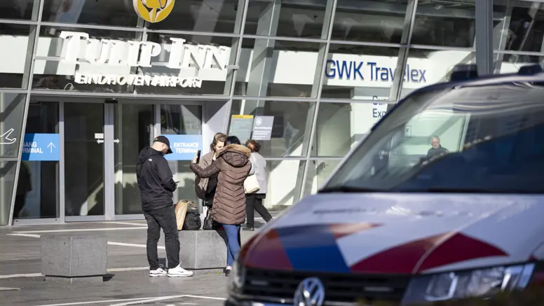 Voertuig van de KMar op Eindhoven Airport, op de achtergrond agenten in burger die met een vrouw praten. 