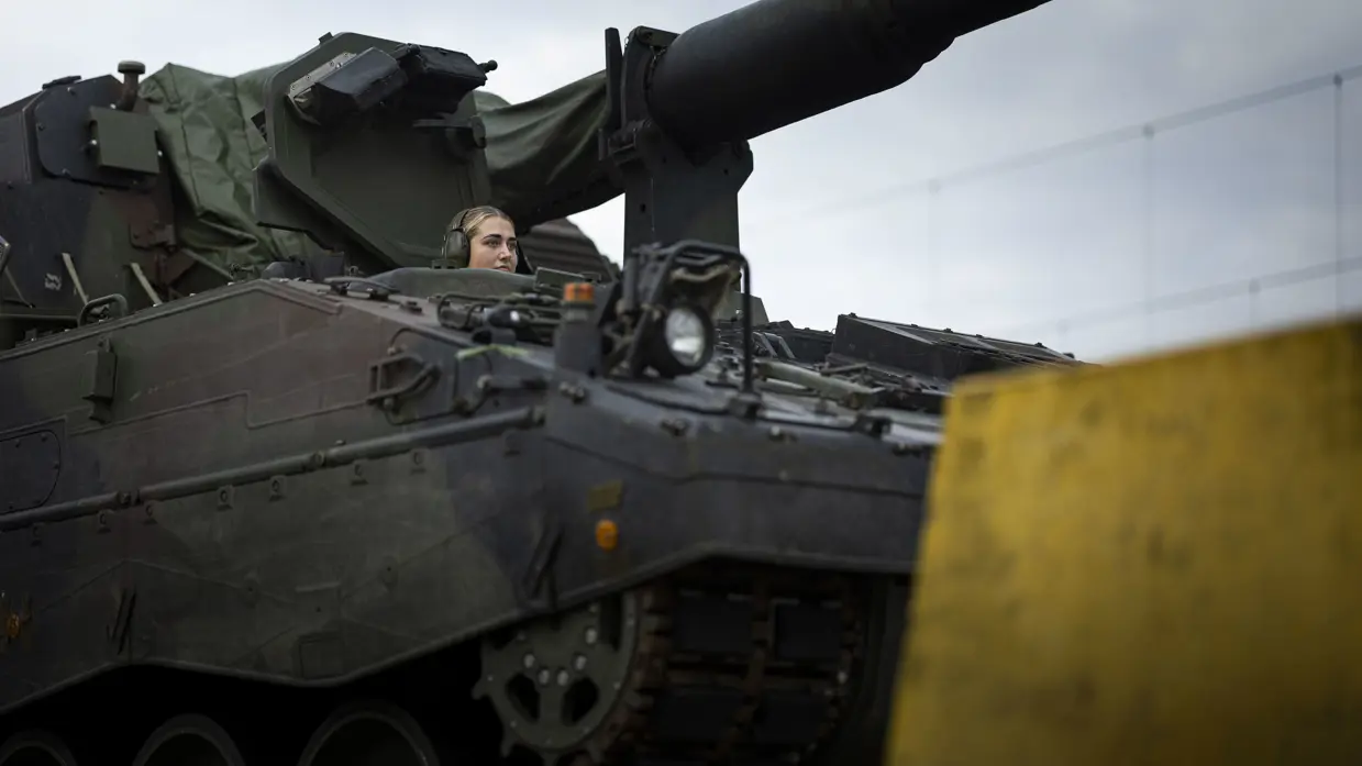 Een vrouwelijke militair bestuurt een pantserhouwitser.
