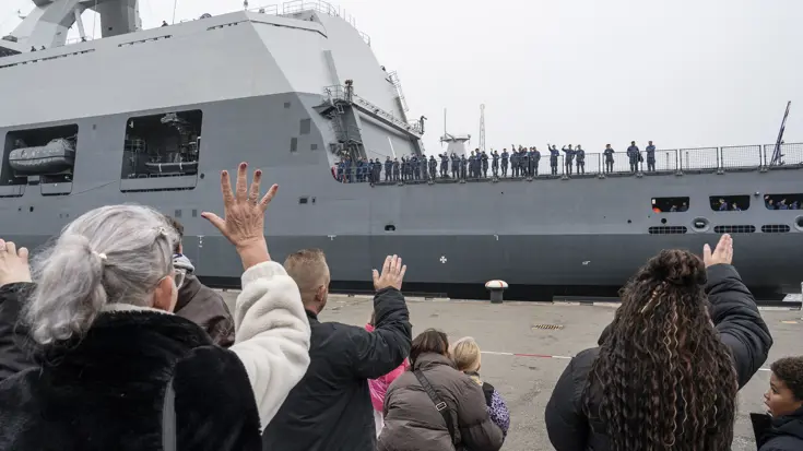Marinepersoneel aan boord van een schip wordt uitgezwaaid.