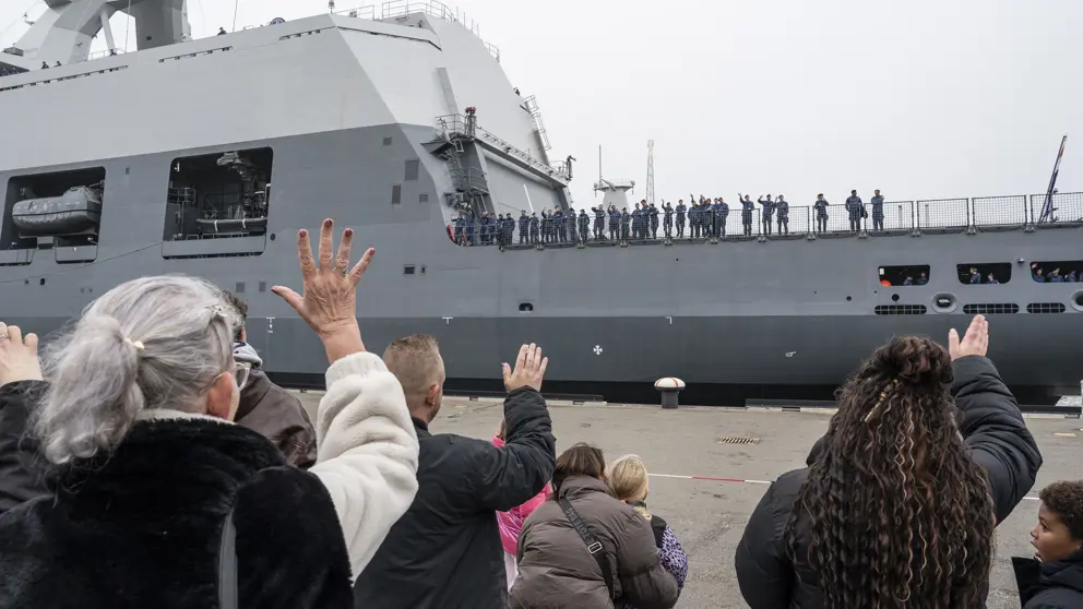 Marinepersoneel aan boord van een schip wordt uitgezwaaid.