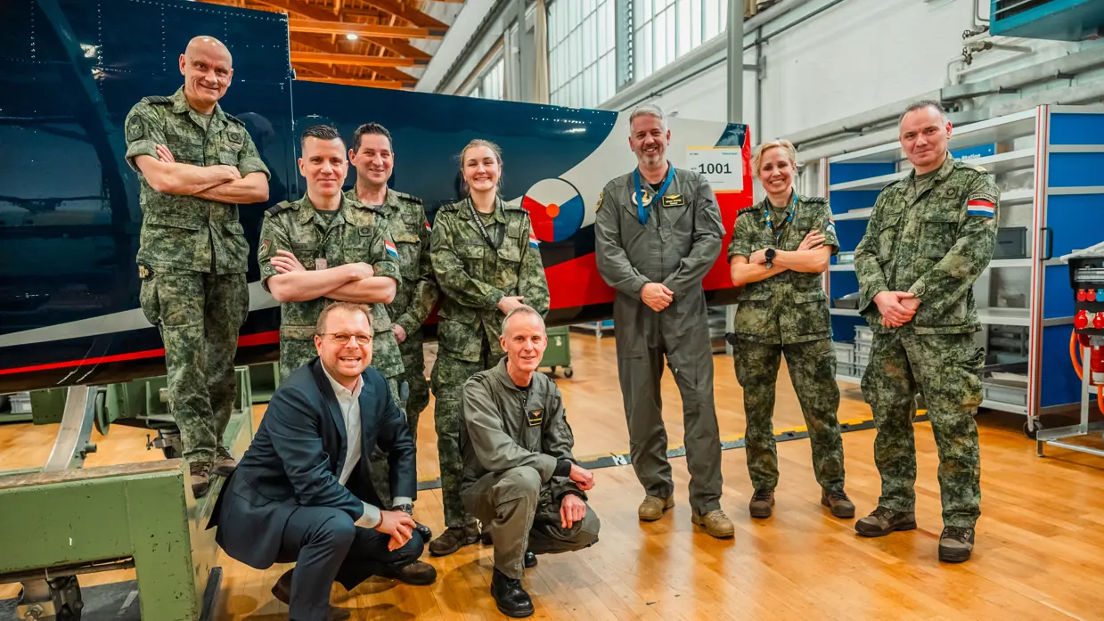 Acht Nederlandse militairen van verschillende eenheden poseren in een hal voor het nieuwe toestel.
