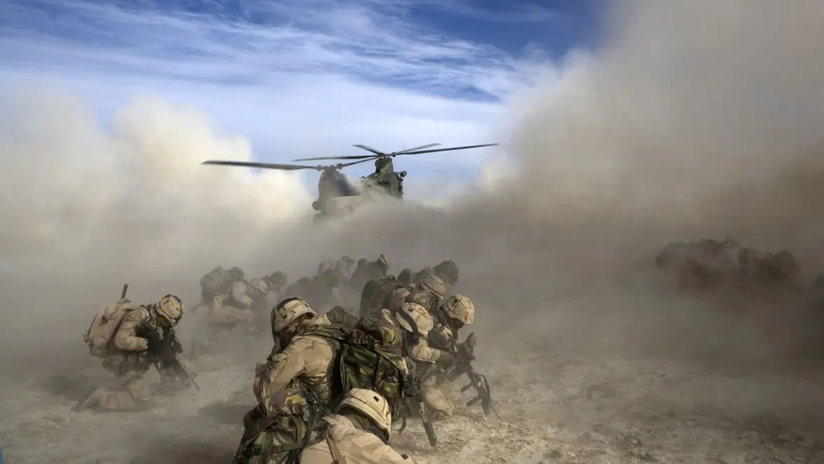  Militairen beschermen zich tegen het opwaaiende fijne zand, veroorzaakt door de dalende Chinook helikopter die ze na hun actie op komt pikken.