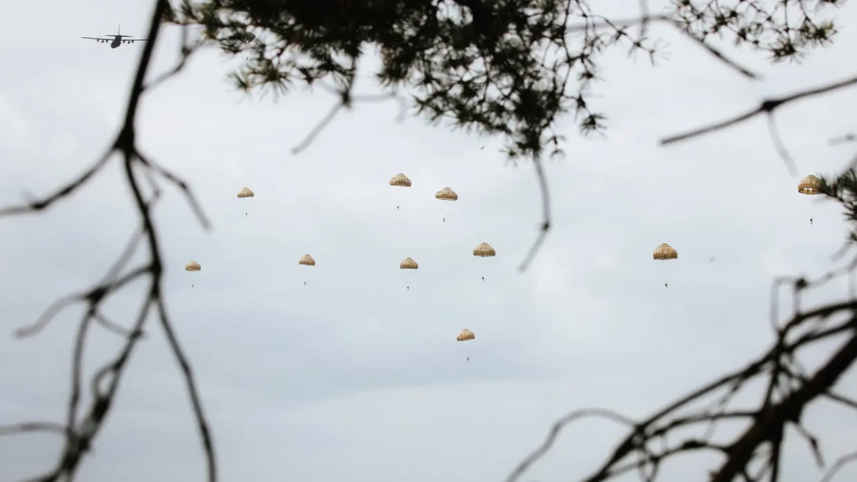 Tussen takken door komen in de lucht parachutisten.