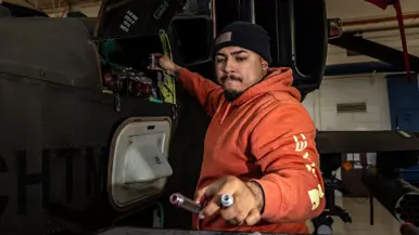 Een Amerikaanse techneut in een oranje trui met capuchon aan het werk aan een Chinook.