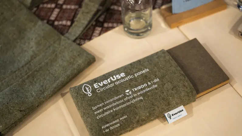 Een groenachtig, textuurrijk akoestisch paneel met de tekst 'EverUse Circular acoustic panels'. Naast het paneel ligt een klein wit kaartje met hetzelfde logo