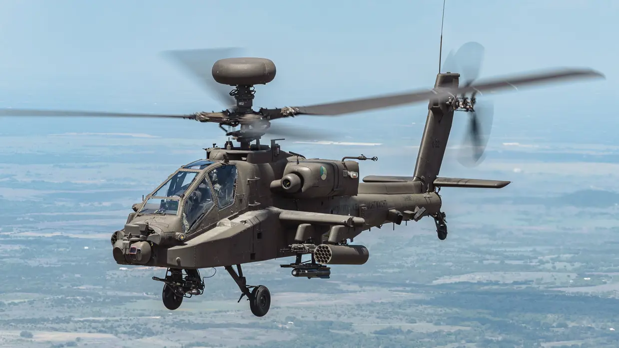 Een Apache, met radarbol bovenop, vliegt boven een landschap.