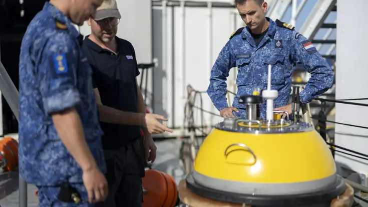 LTZ1 Leon en sergeant Matthijs met een medewerker van TNO bij de gele gateway buoy. De drie kijken naar het systeem en zijn daarover in gesprek.