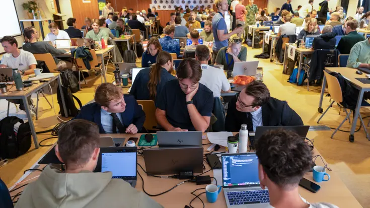 Overzicht van een grote ruimte met veel tafels waaraan mensen zitten achter een laptop.