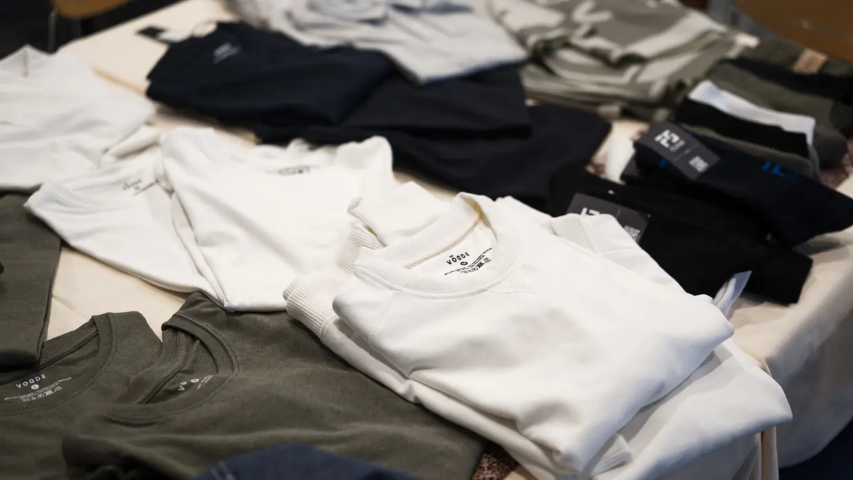 Een tafel met verschillende stapels zorgvuldig gevouwen kleding in diverse kleuren zoals wit, grijs, zwart en olijfgroen.
