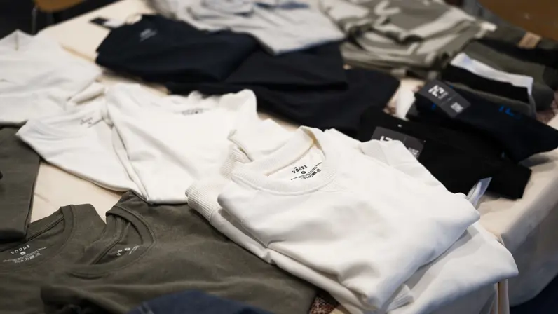 Een tafel met verschillende stapels zorgvuldig gevouwen kleding in diverse kleuren zoals wit, grijs, zwart en olijfgroen.