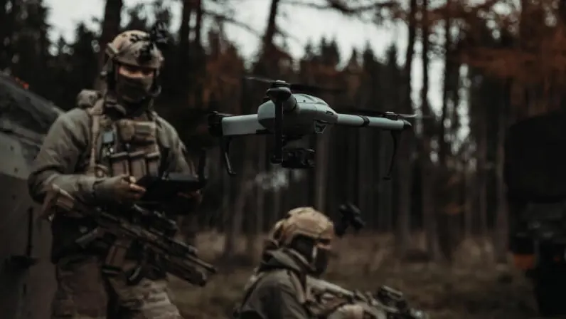 Een militair staat in het bos. Voor hem vliegt een drone, die hij bedient.  