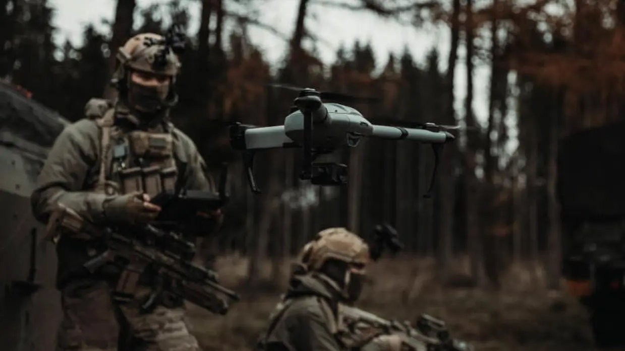 Een militair staat in het bos. Voor hem vliegt een drone, die hij bedient.  
