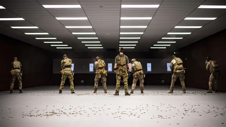 Zes militairen van het KCT, naast elkaar op een overdekte schietbaan. Achter hen ligt de vloer bezaaid met hulzen.