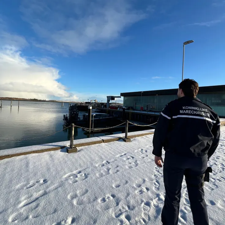 Marechaussee kijkt uit over besneeuwde haven.