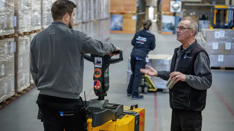 Teamleider Ron in gesprek met een collega. Laatstgenoemde bestuurt een gele palletwagen.