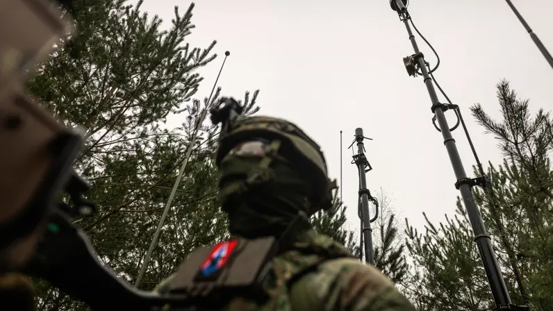 Gemaskerde militair in het veld met antennes op de achtergrond
