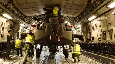 Militairen staan in het laadruim van een vrachtvliegtuig en duwen een Apache naar buiten.