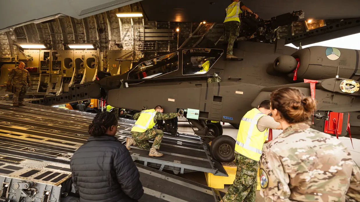 Majoor Saskia (rechts) kijkt hoe militairen in gele hesjes een Apache uit het laadruim duwen.