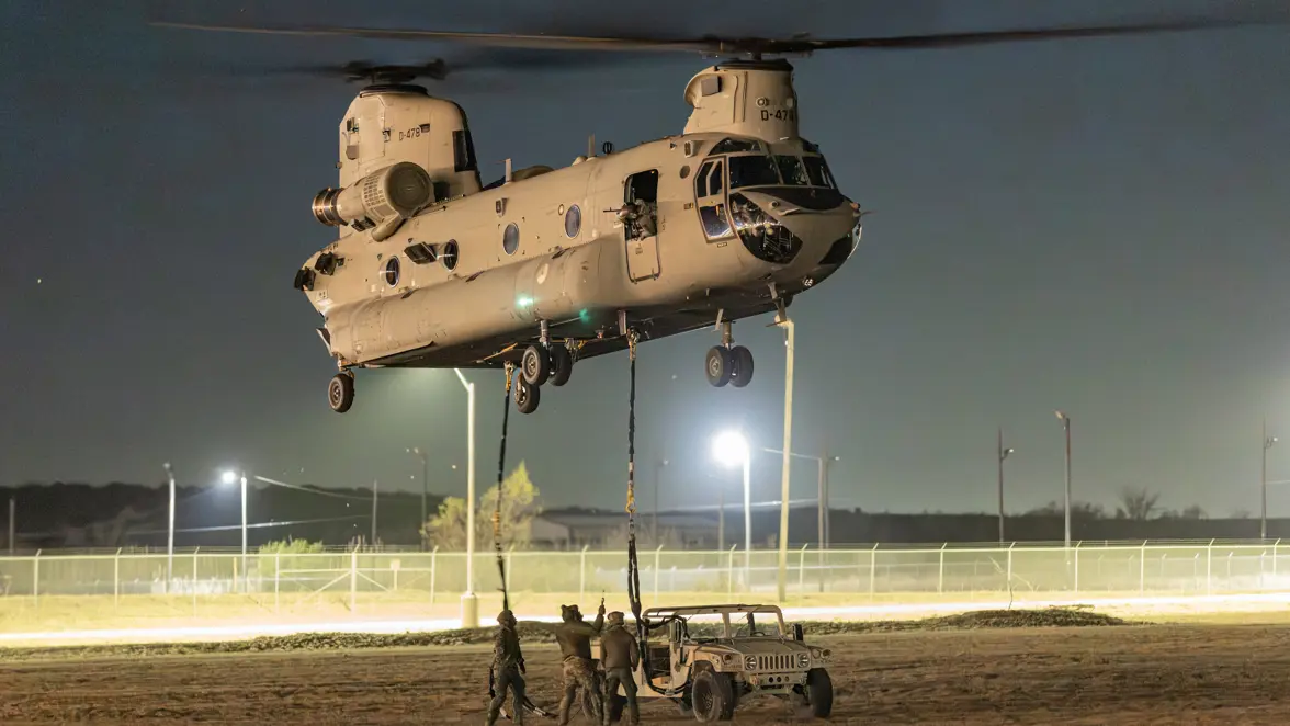 Alt-tekst: Bij duisternis koppelen militairen een voertuig aan als slingload onder een Chinook.  