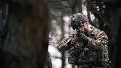 een Nederlandse militair in gevechtsuitrusting richt zijn geweer richting de camera, op zijn vest zit het embleem van 1GNC. 
