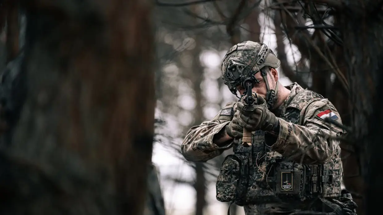 een Nederlandse militair in gevechtsuitrusting richt zijn geweer richting de camera, op zijn vest zit het embleem van 1GNC. 