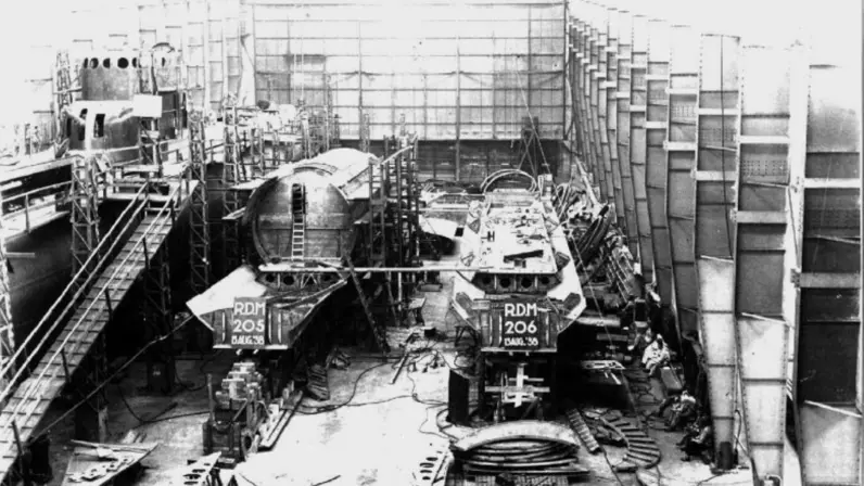 Een scheepswerf met deels afgebouwde scheepsrompen, gemerkt RDM 205 en RDM 206. Steigers, ladders en materiaal omringen de rompen.&nbsp;