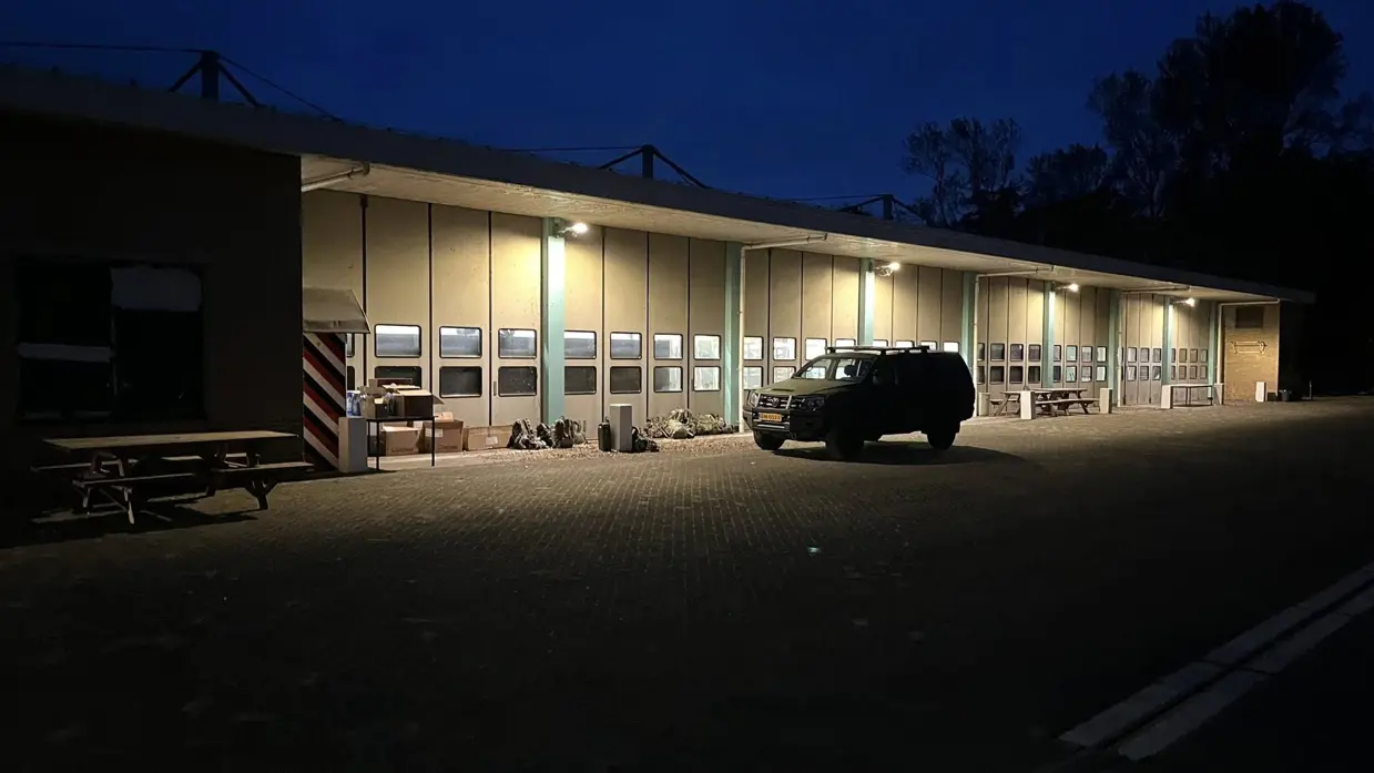 Alttekst: Een militair voertuig staat in het donker geparkeerd voor een loods.