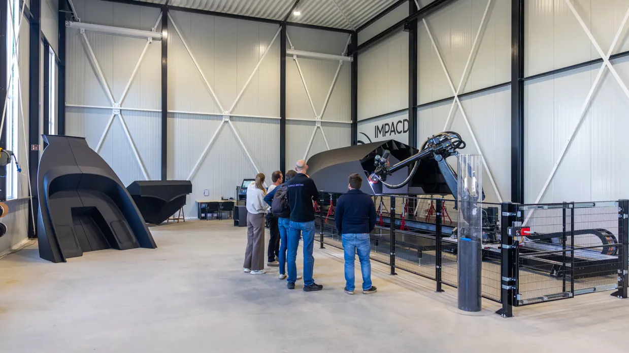  Vijf mensen kijken in fabriekshal naar de 3D-geprinte boot.