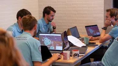 Vijf medewerkers van de Marechaussee zitten aan een tafel achter een eigen laptop te turen naar het scherm.