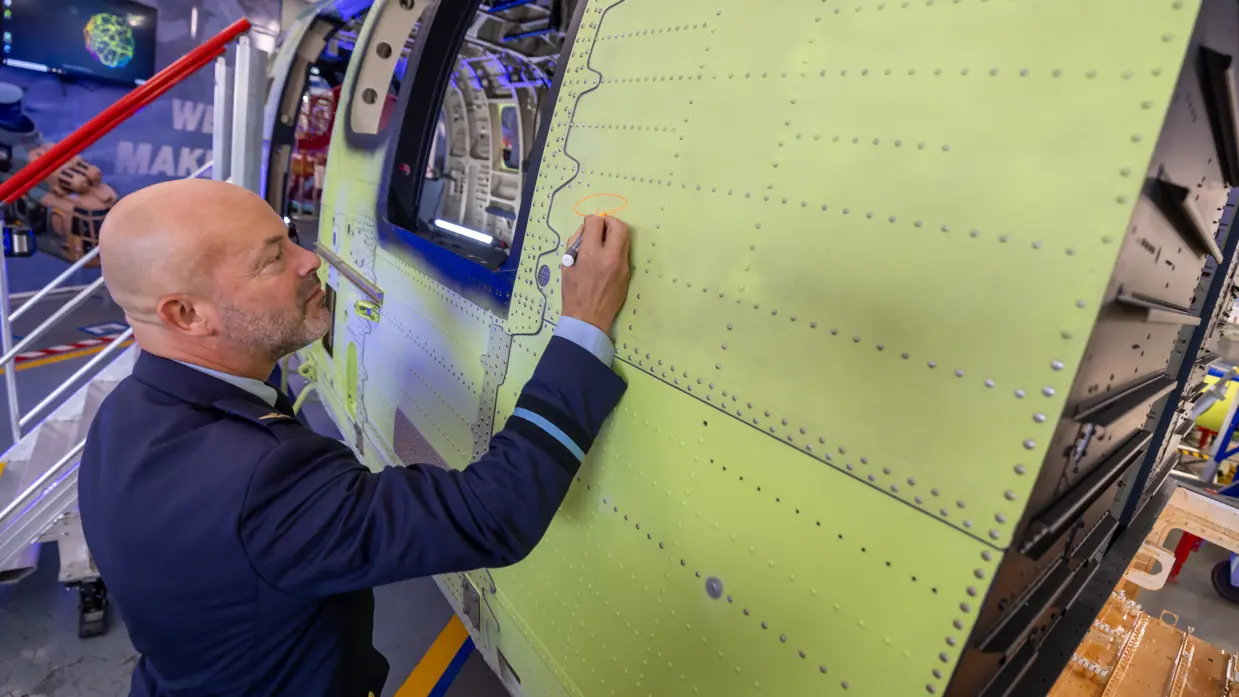 Een man in donkerblauw militair uniform zet een handtekening op het helikopterframe.