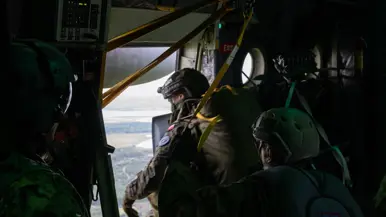In een vliegtuig kijken 3 militairen met helmen door de open deur naar het landschap beneden.