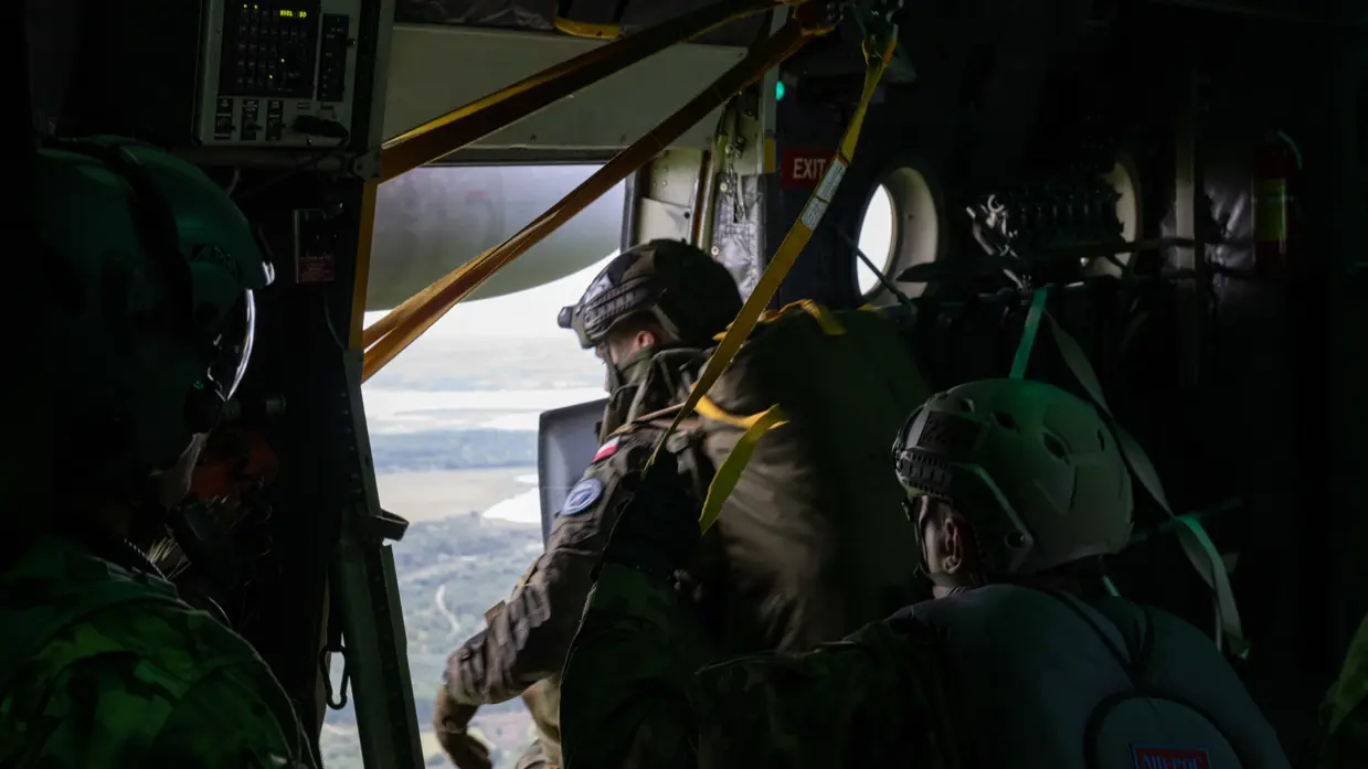 In een vliegtuig kijken 3 militairen met helmen door de open deur naar het landschap beneden.