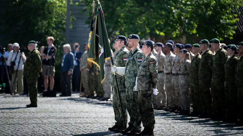 Drie militairen met het vaandel van 1GNC staan in de houding tijdens de commando-overdacht. Om hen heen staan militairen uit diverse landen opgesteld.