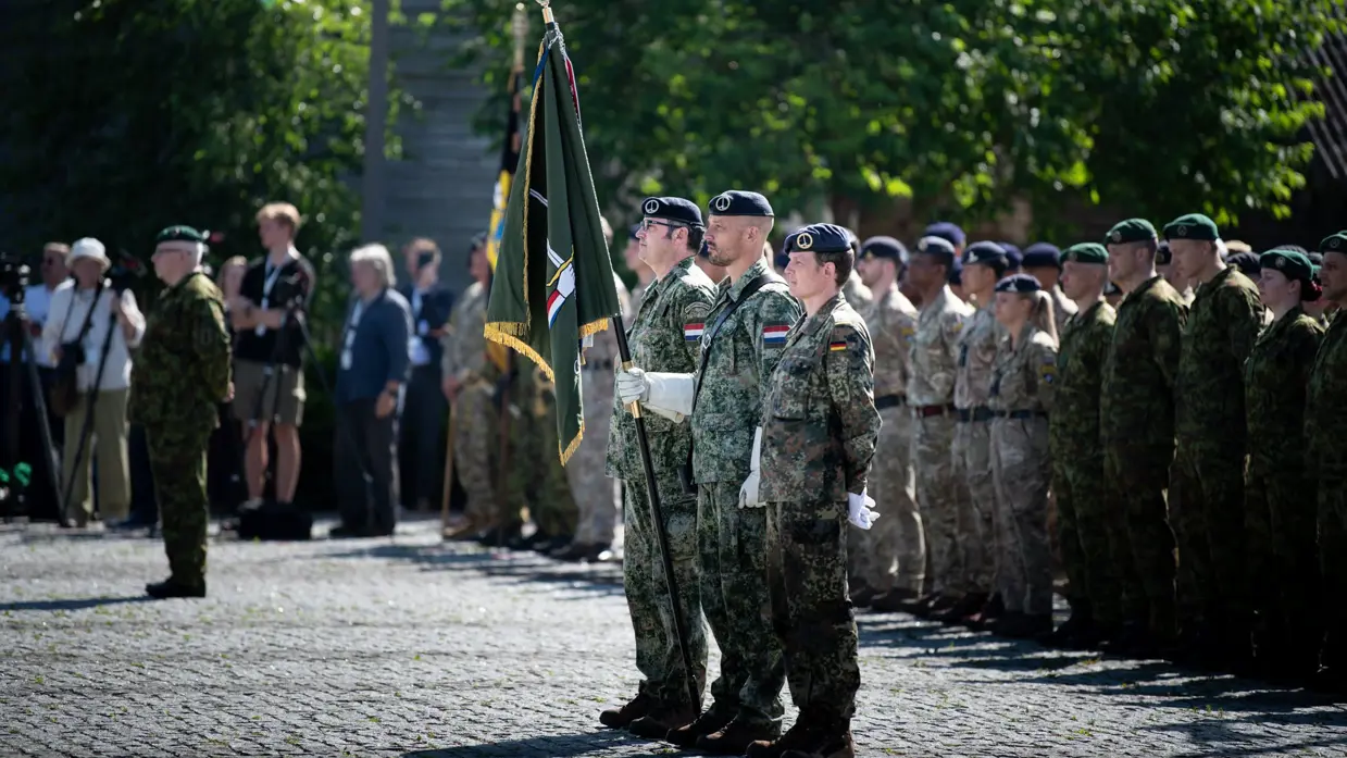Drie militairen met het vaandel van 1GNC staan in de houding tijdens de commando-overdacht. Om hen heen staan militairen uit diverse landen opgesteld.