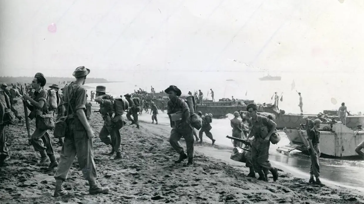 Een zwart-wit foto met militairen die aan land komen vanaf boten.