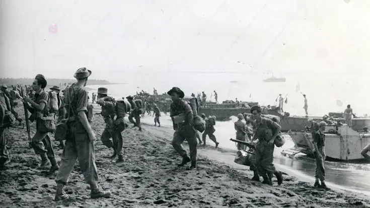 Een zwart-wit foto met militairen die aan land komen vanaf boten.