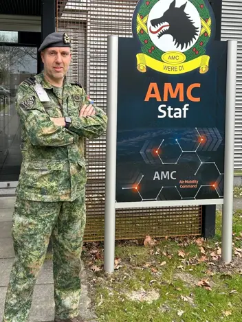 Portretfoto van luitenant-kolonel Misja Woudt. Naast hem het logo van het Air Mobility Command in Eindhoven.