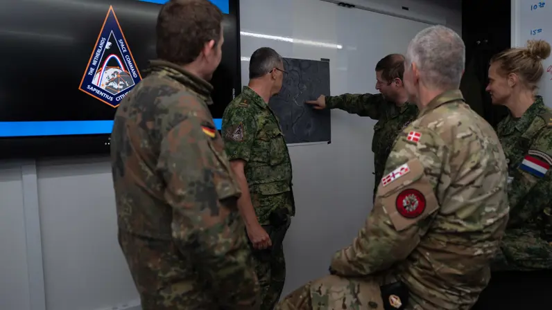 Een groepje militairen uit verschillende landen kijkt naar een briefing van een Nederlandse collega.