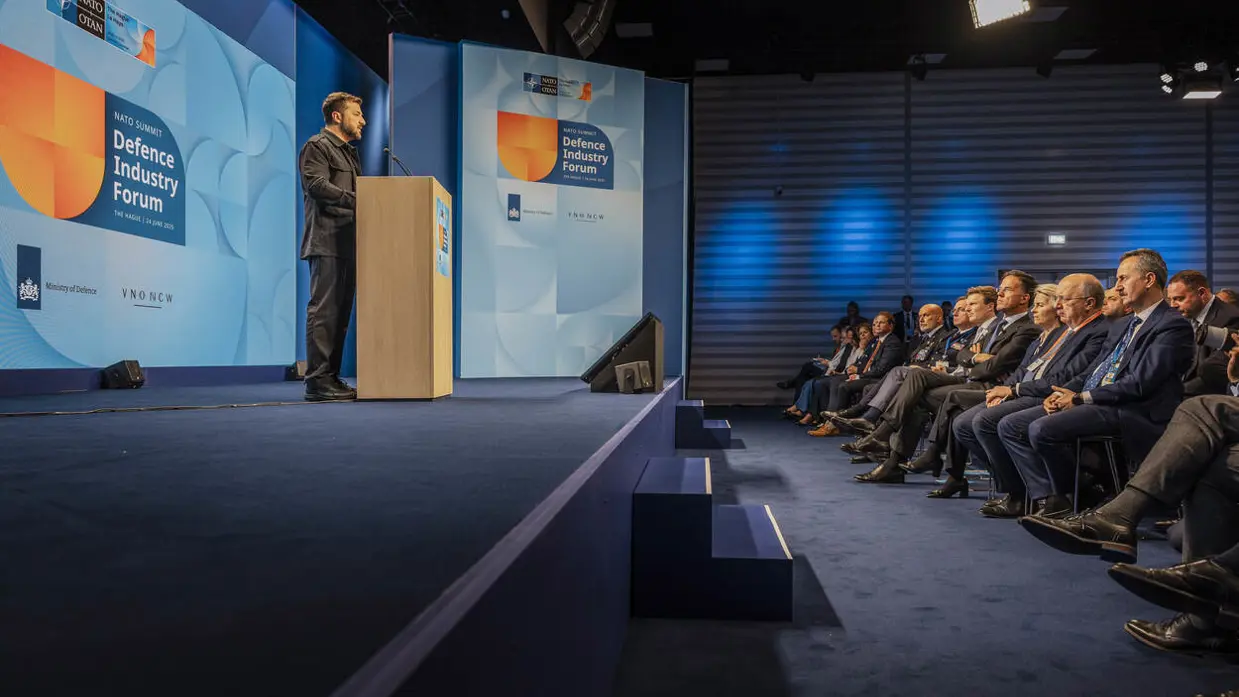 Man achter katheder spreekt volle zaal toe.