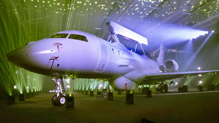 Foto de Saab GlobalEye, schuin van voren op grond in een hangar met paars gekleurde lampen.