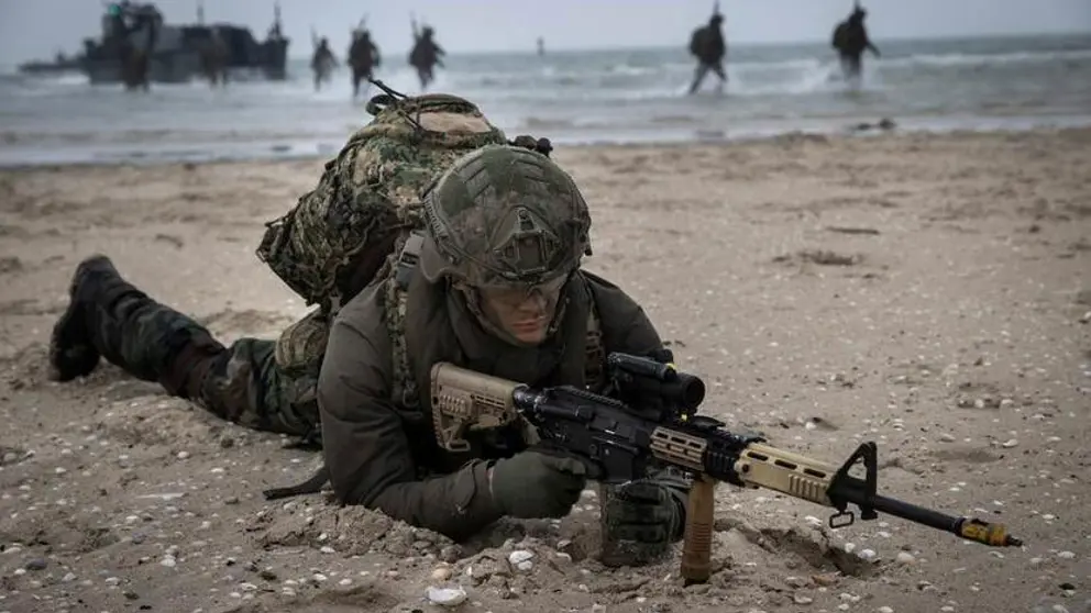 Militair ligt tijdens oefening met wapen gericht op zijn buik op een strand.